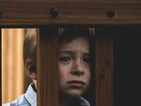 Sad kid peering through a banaster - Our Kids' Mental Well-Being.