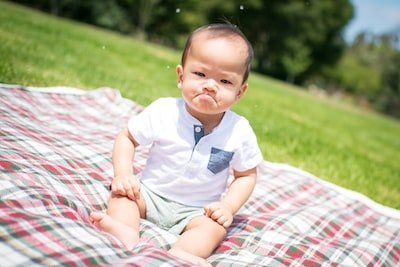 8 ways to help children regulate their emotions. - a baby on a blanket in a park with a pout on his face.
